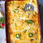 Spatula in a casserole dish removing chicken enchiladas topped with a creamy cheese sauce.