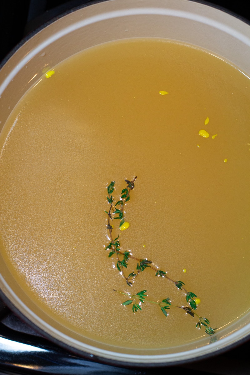 Stockpot filled with chicken broth, topped with fresh thyme springs. 