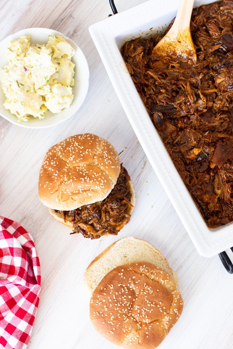 Pulled pork barbecue sandwiches on a table, side of potato salad.