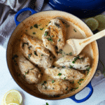 A dutch oven containing 6 chicken breasts topped with basil and lemon slices.