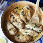 Pan seared chicken breasts in a skillet topped with a garlic cream sauce, topped with basil and lemon.
