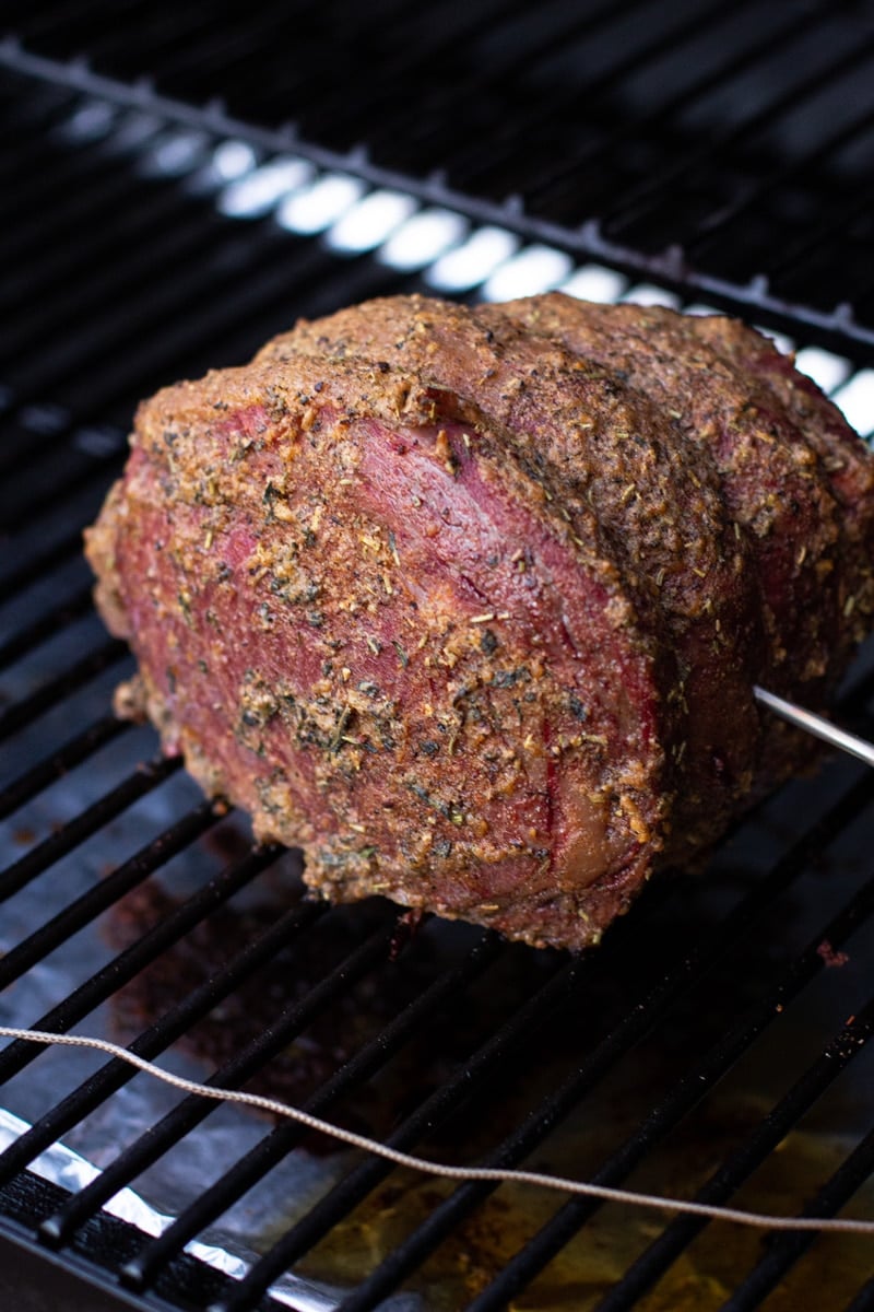 Seasoned prime rib on a smoker, digital thermometer in center of meat. 