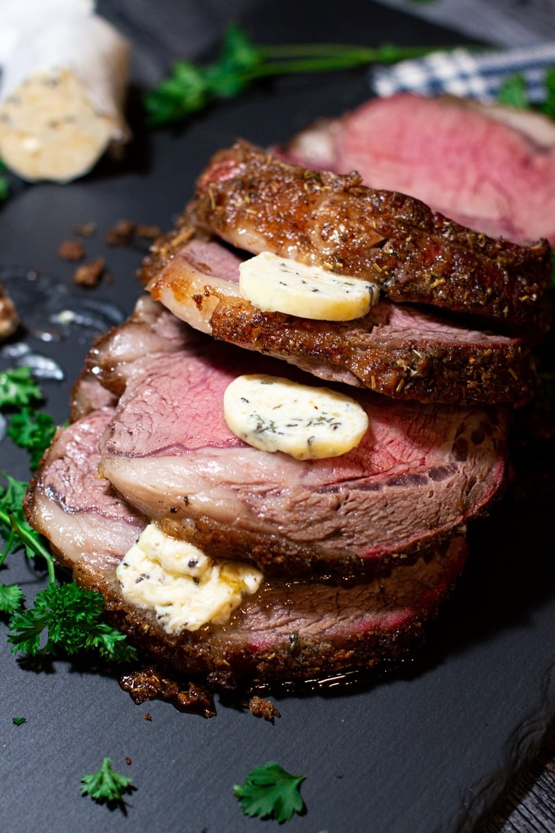 Sliced smoked prime rib roast topped with slices of herb compound butter.