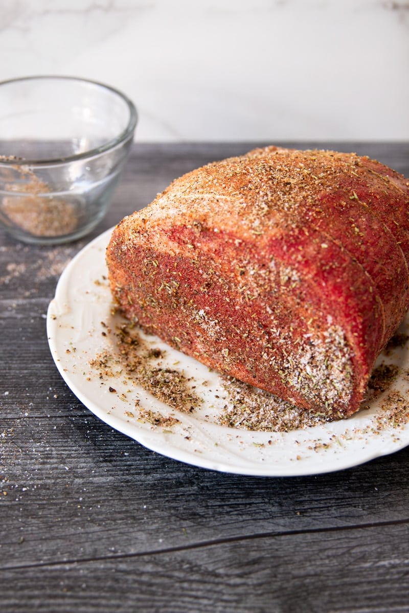 Seasoned prime rib roast on a plate sitting on a counter. 