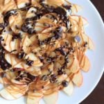 A plate of apple nachos topped with chocolate chips and caramel.
