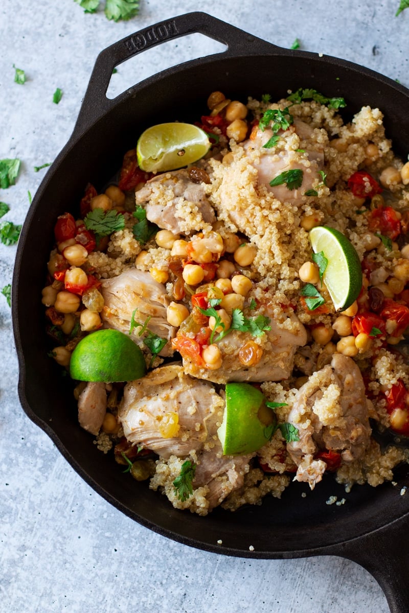 Cast iron skillet with chicken, chickpeas, tomatoes, limes, and parsley.