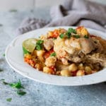White bowl containing pan seared chicken thighs, chickpeas, couscous, and tomatoes.