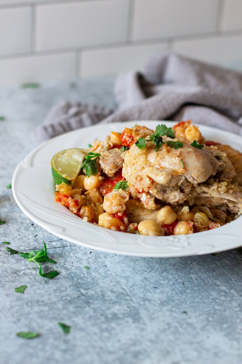 White bowl containing pan seared chicken thighs, chickpeas, couscous, and tomatoes. 