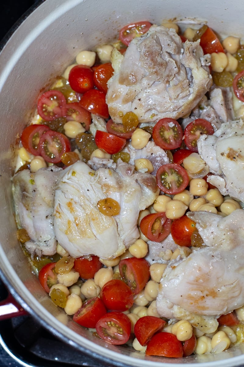 Dutch oven containing cooked chicken thighs with chickpeas and sliced tomatoes. 