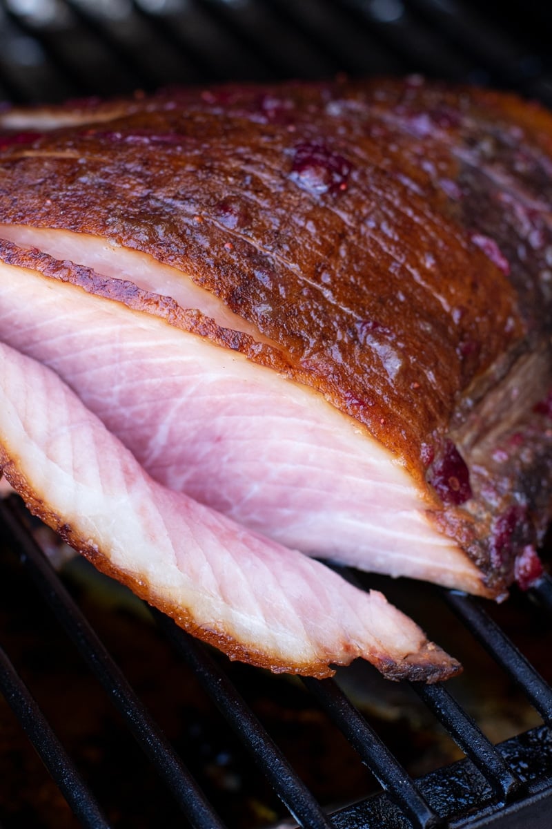 Sliced ham that has been smoked sitting on the grill grates of a smoker.