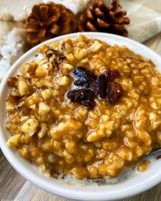 White bowl containing oatmeal topped with dried raisins. 