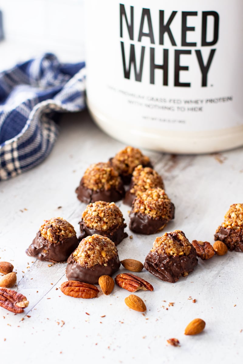 Peanut butter protein balls dipped in chocolate on a table, Naked Whey protein powder in background.