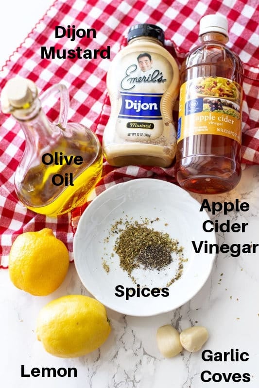 Dijon mustard, Olive oil, Apple cider vinegar, Spices, Garlic gloves ,and Lemon laid out on a table.