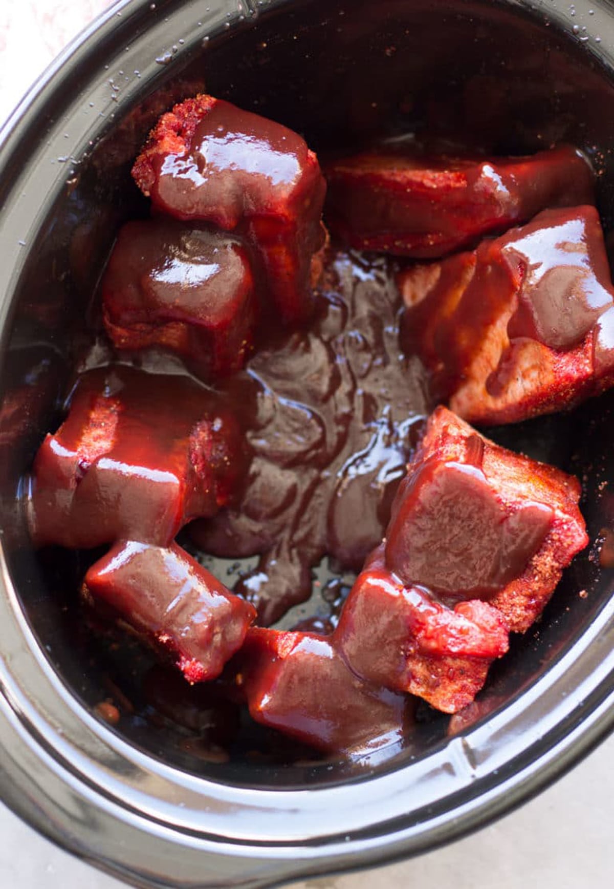 Beef short ribs in a slow cooker covered in BBQ Sauce.