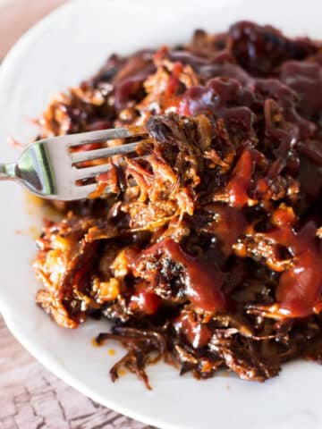 Pulled beef short ribs covered in BBQ sauce and person eating with a fork.