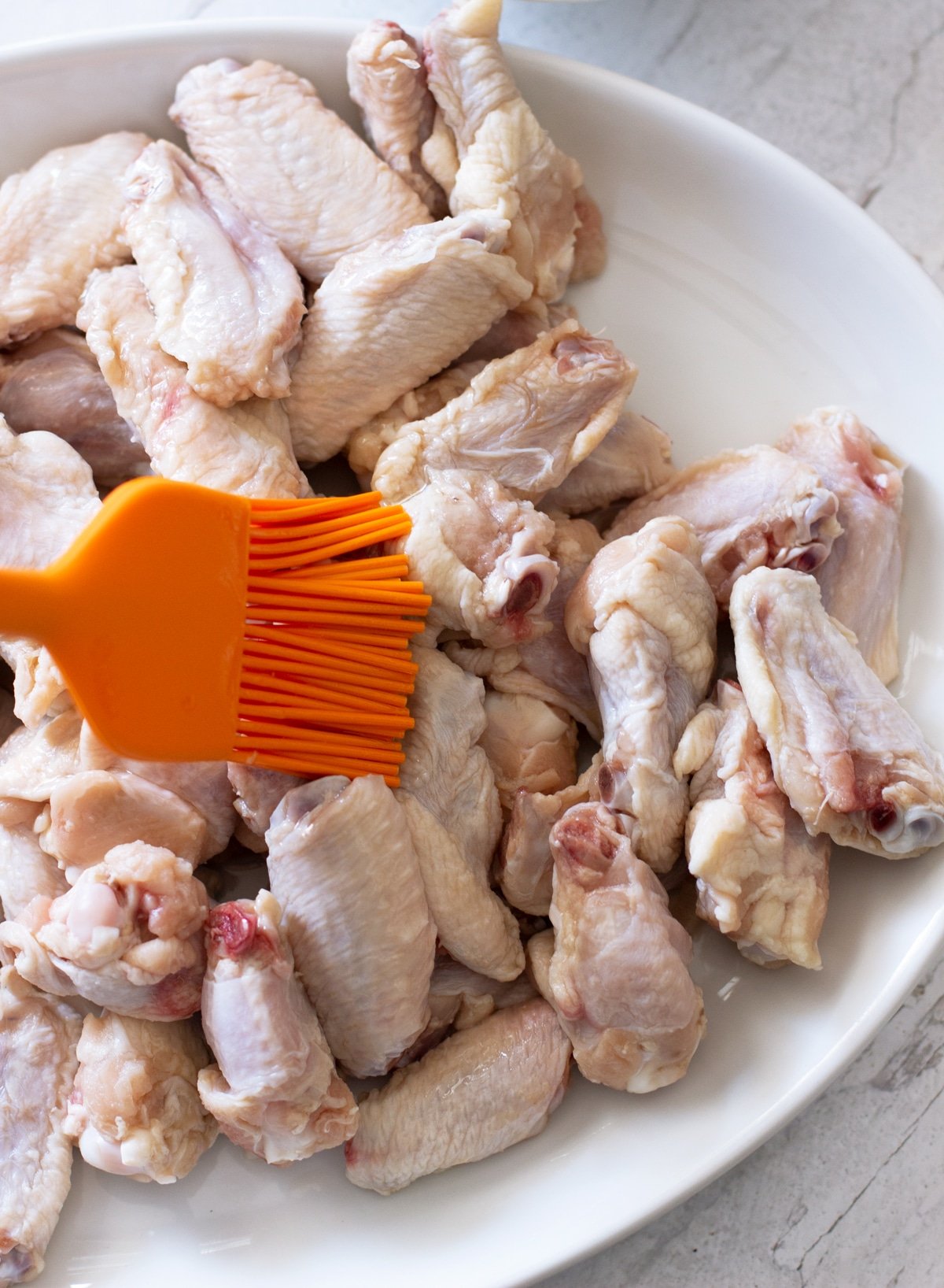Person basting chicken wings with olive oil.
