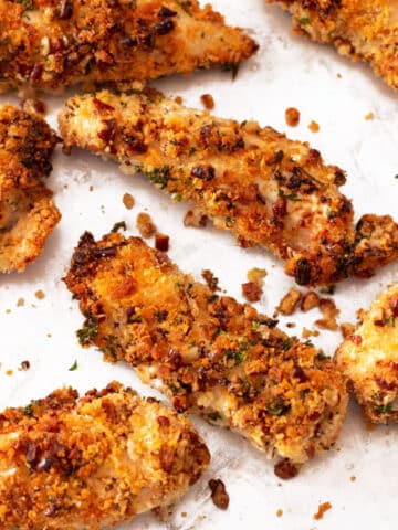 Sheet pan containing 7 air fryer chicken tenders coated in a pecan crust.