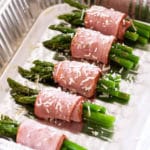 Aluminum pan containing asparagus wrapped in turkey bacon topped with Parmesan cheese.