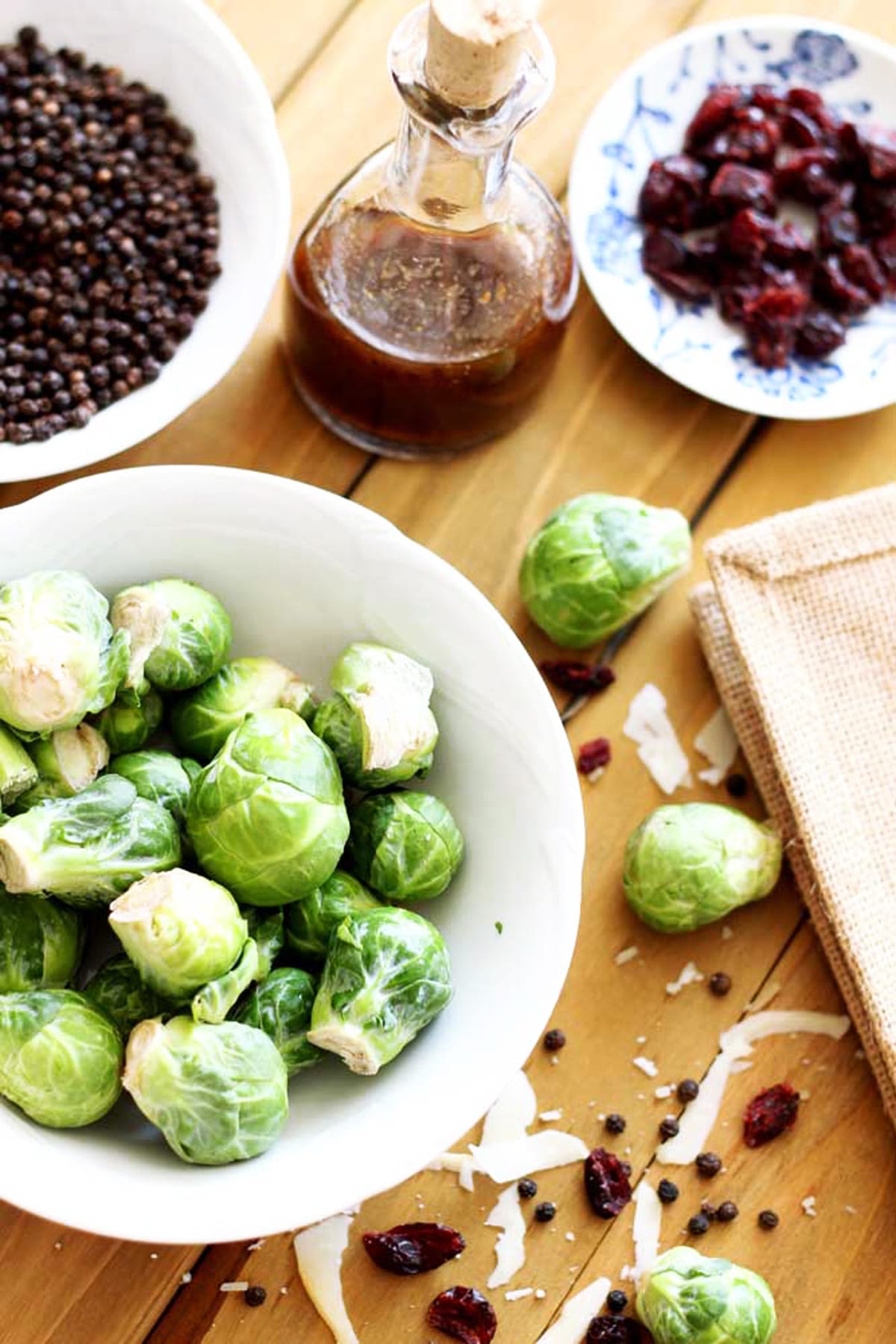 White bowl containing Brussel Sprouts, Parmesan cheese, cranberries and vinaigrette dressing on wooden table. 