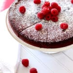 Sliced Flourless Chocolate Torte sitting on a cake dish topped with powdered sugar and fresh raspberries.