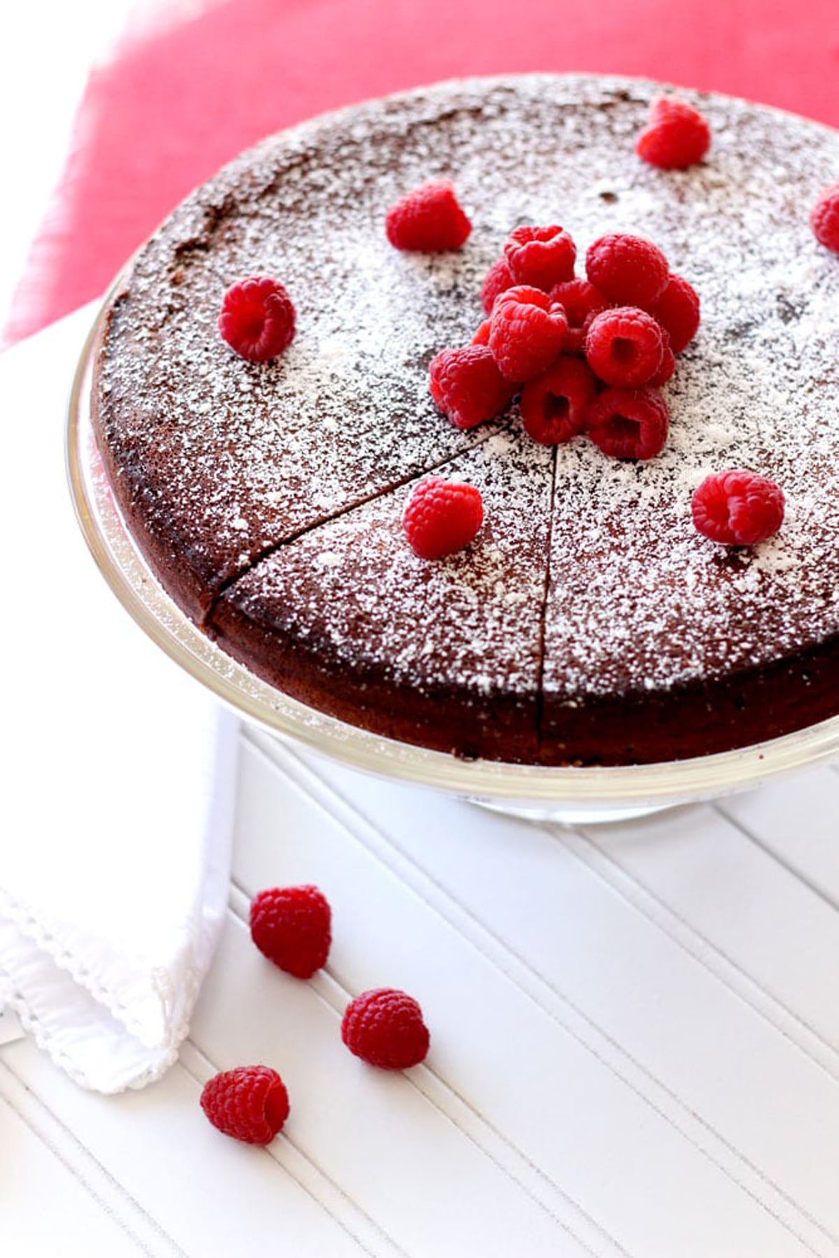 Sliced Flourless Chocolate Torte sitting on a cake dish topped with powdered sugar and fresh raspberries.