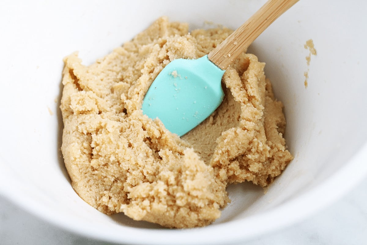 White bowl containing Cookie Dough, blue spatula in bowl.