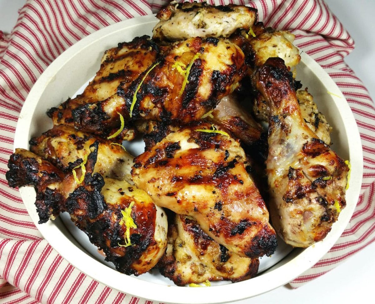 8 pieces of grilled chicken thighs and legs in a brown bowl sitting on a red and white napkin, topped with lemon zest.