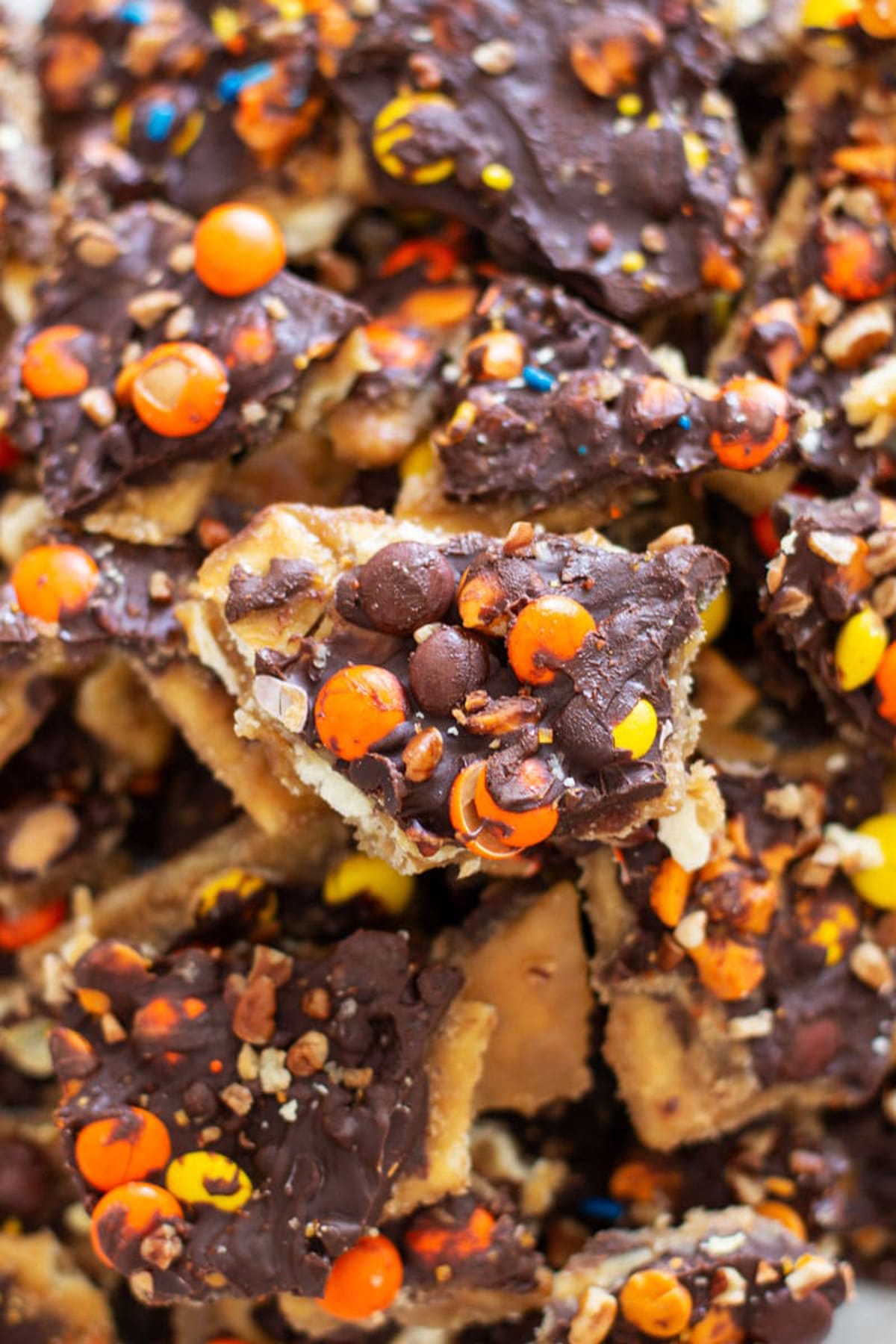 White plate containing Halloween Bark Candy topped with reese's pieces, pecans and melted chocolate.