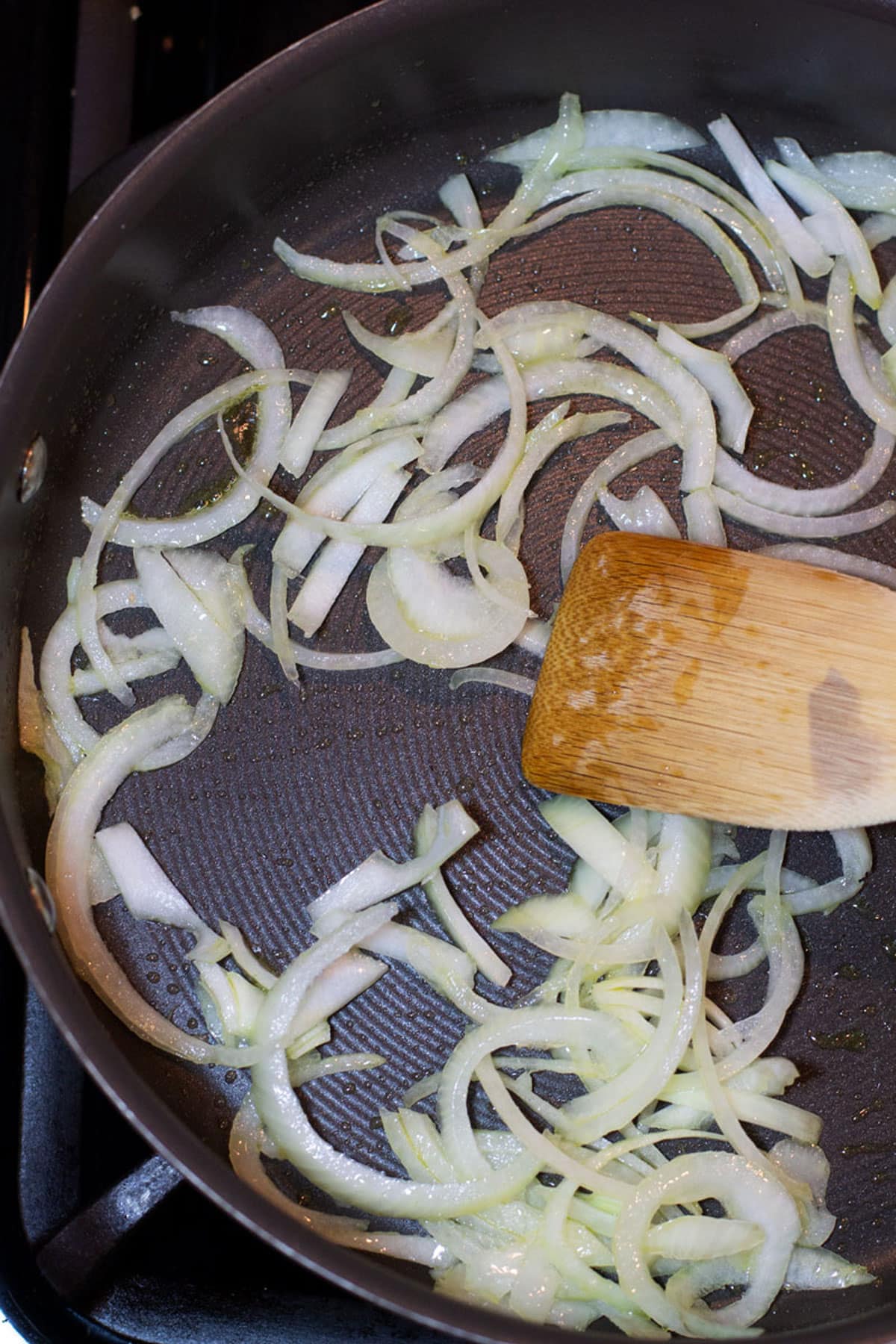 Spatula sauteing onion in a skillet heated with olive oil.