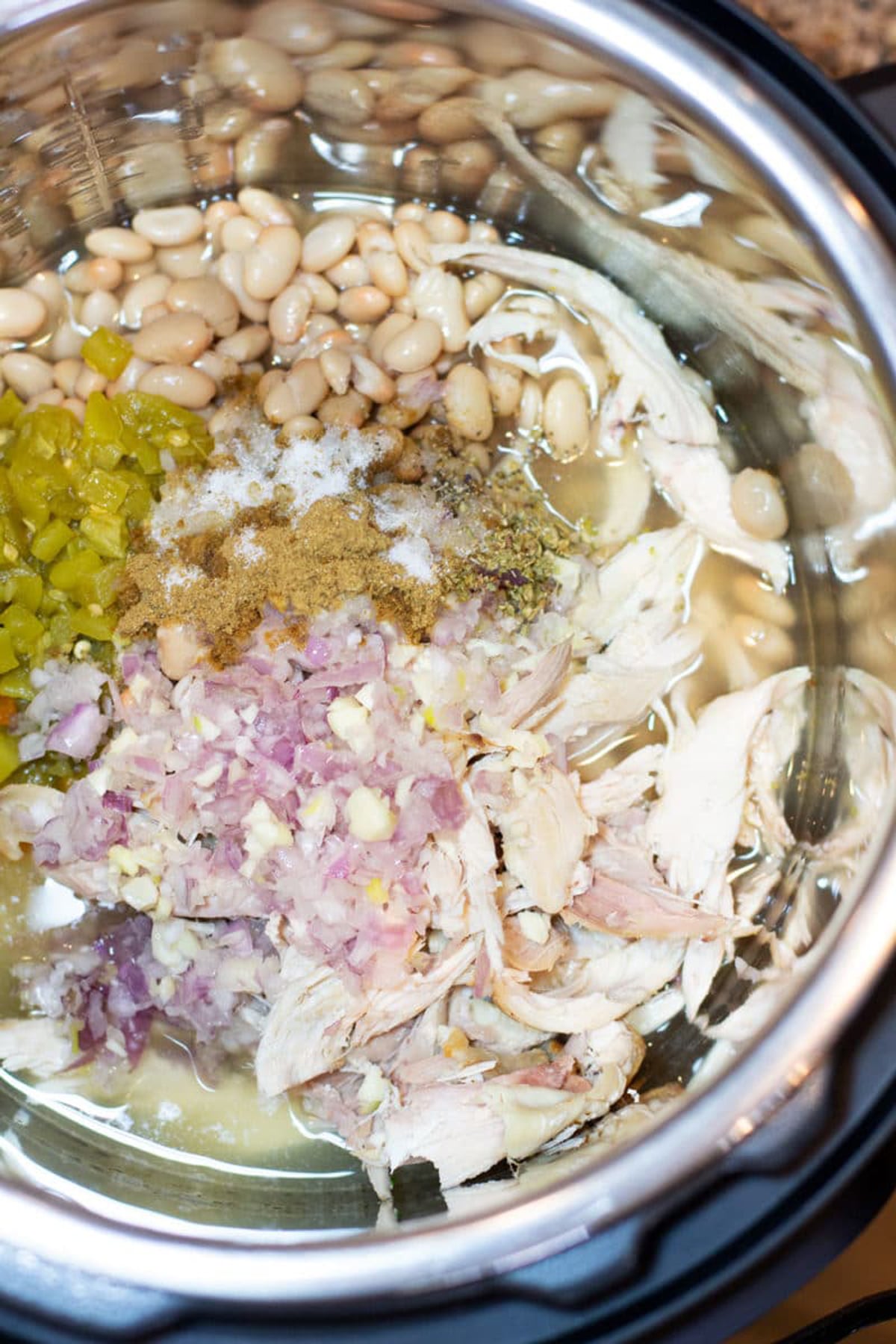 Instant Pot containing white beans, shredded chicken, green chilis, shallot and seasonings.