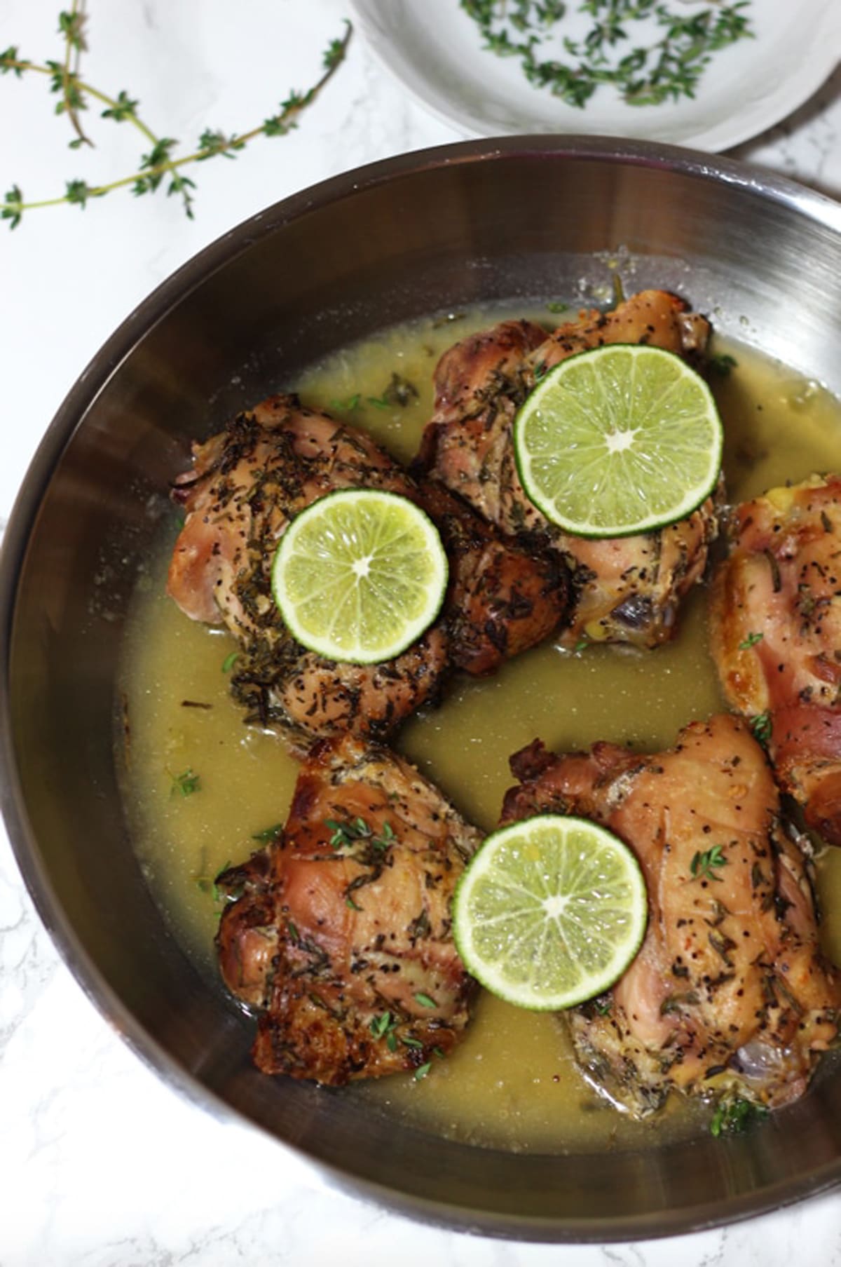Five chicken thighs baked in a lemon garlic thyme and rosemary sauce, topped with fresh lemon slices.