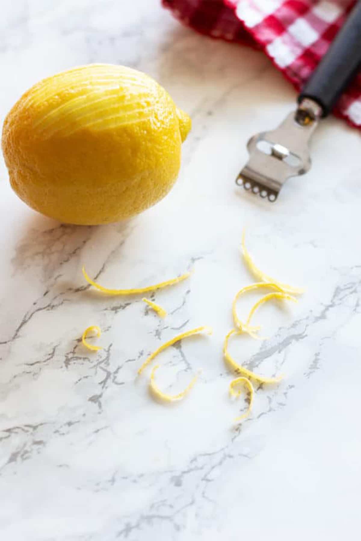 Lemon zest sitting on a white marble table, lemon in background.