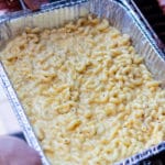 Aluminum pan of macaroni and cheese being placed in a smoker.