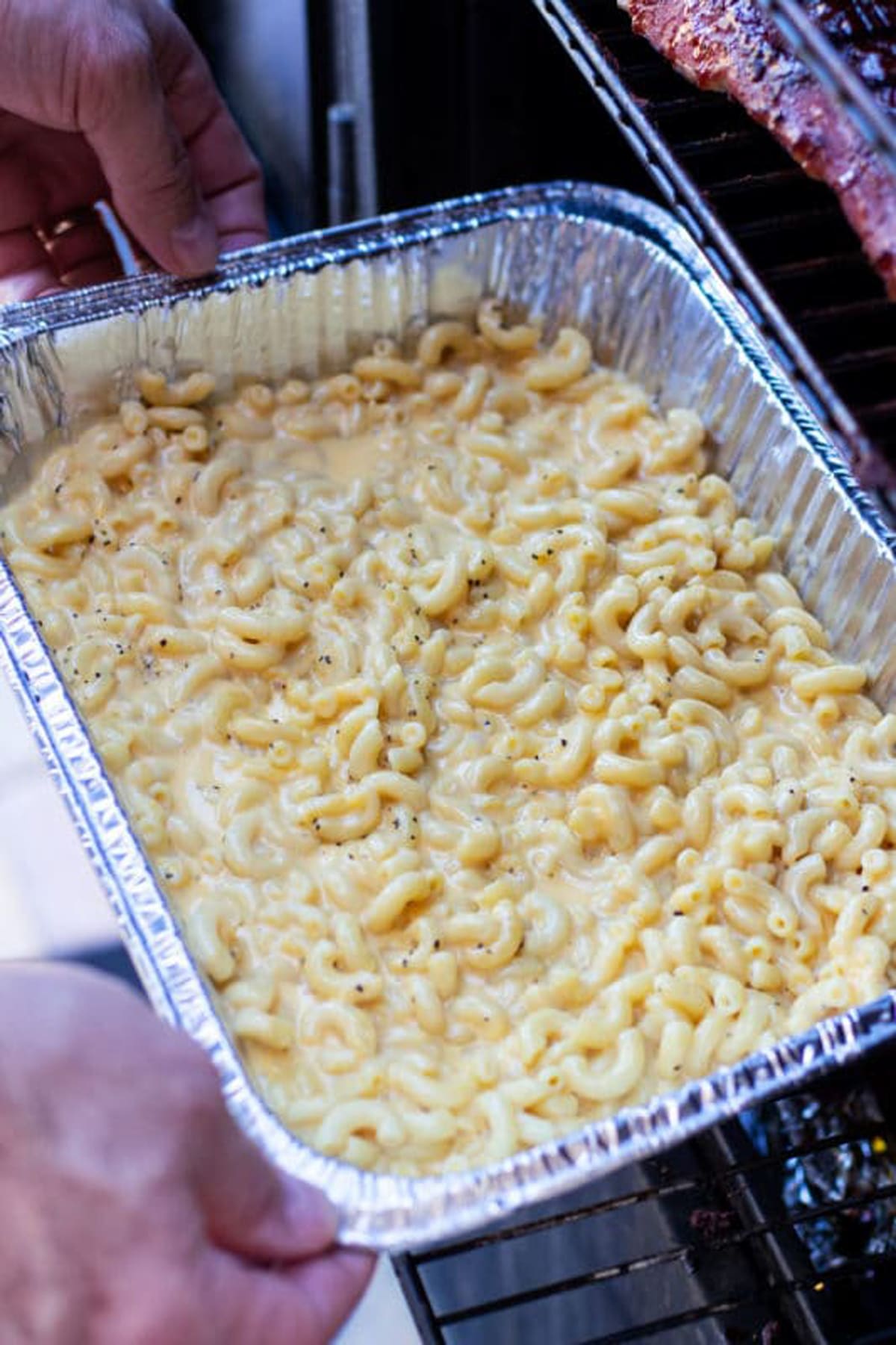 Aluminum pan of macaroni and cheese being placed in a smoker.