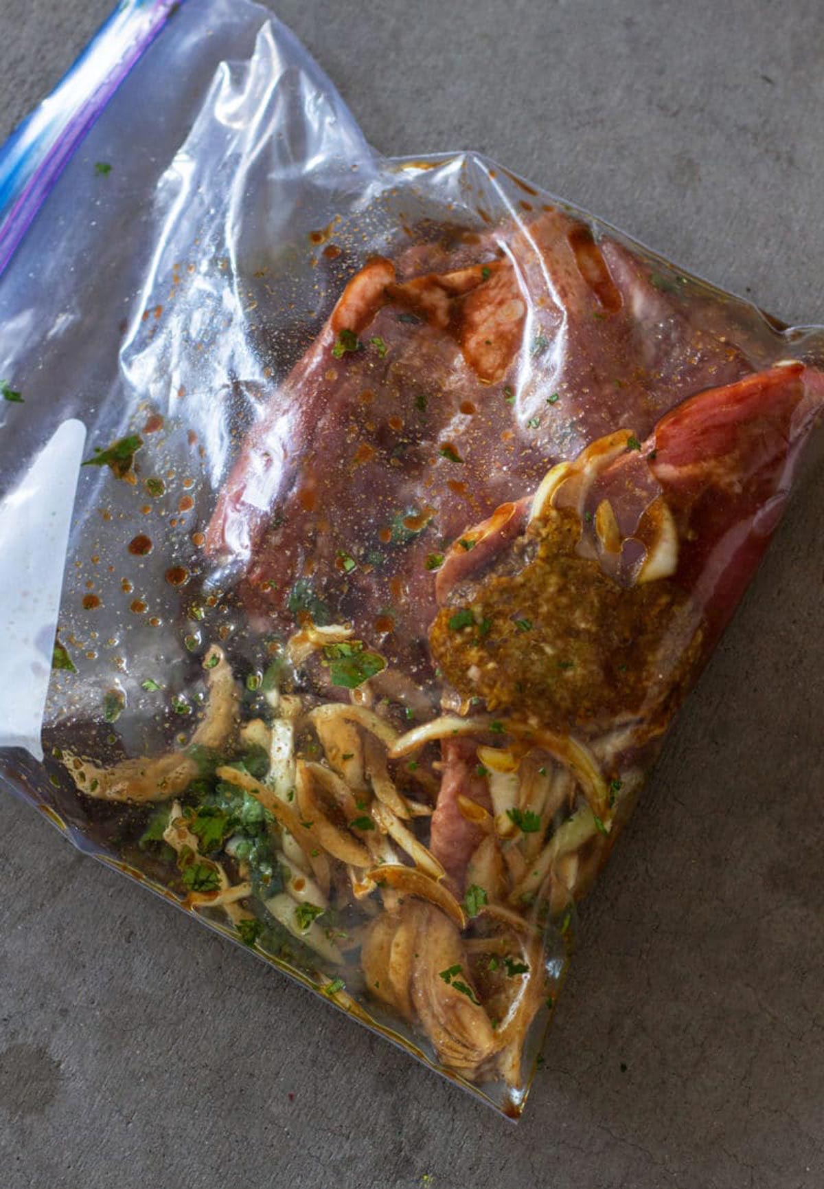 Gallon Ziplock bag containing a flank steak marinating in a garlic lime sauce.