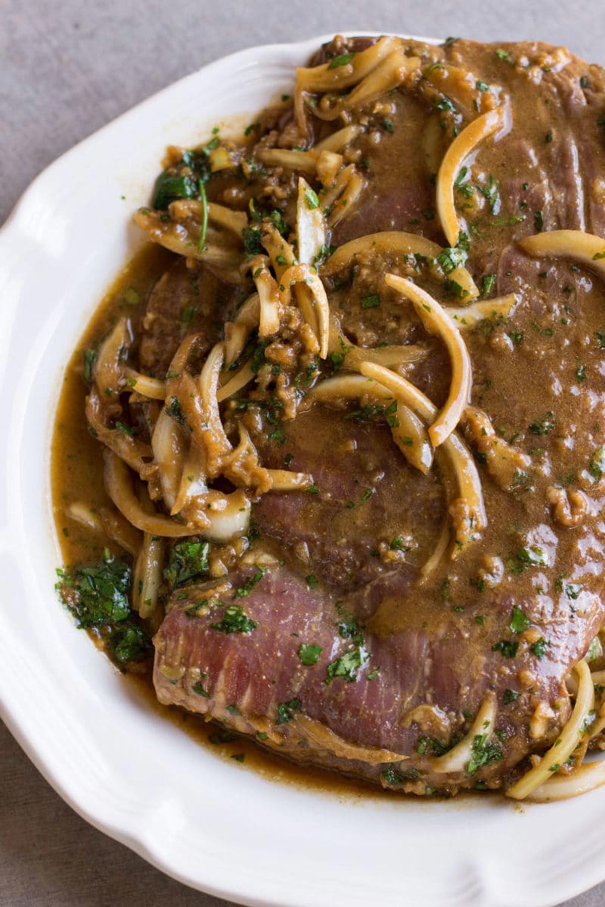 Flank steak covered in a garlic lime marinade topped with sliced onions and cilantro.