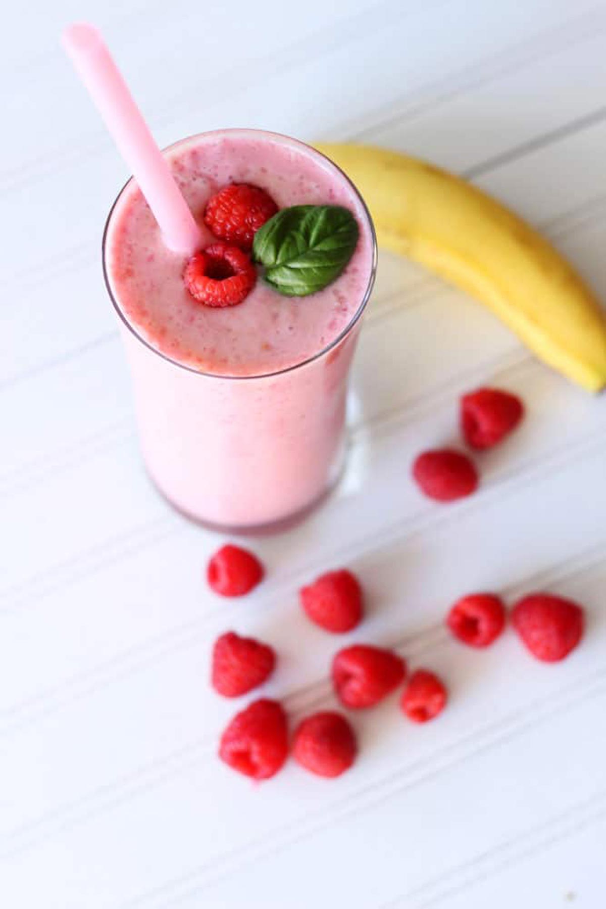 Glass containing a raspberry banana smoothie topped with 2 raspberries and a mint spring. 