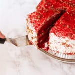 Person slicing a Red Velvet Cake and getting ready to serve with a spatula.