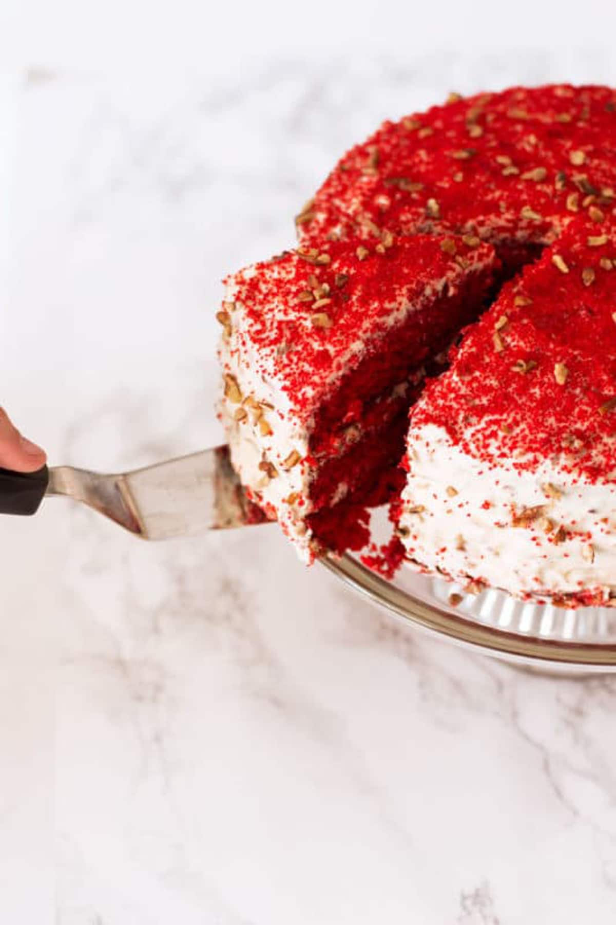 Person slicing a Red Velvet Cake and getting ready to serve with a spatula. 