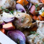 White dish containing roasted chicken with sweet potatoes, carrots, and red onions topped with fresh thyme.