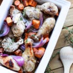 White dish containing roasted chicken drumsticks with sweet potatoes, carrots, and red onions topped with fresh thyme.