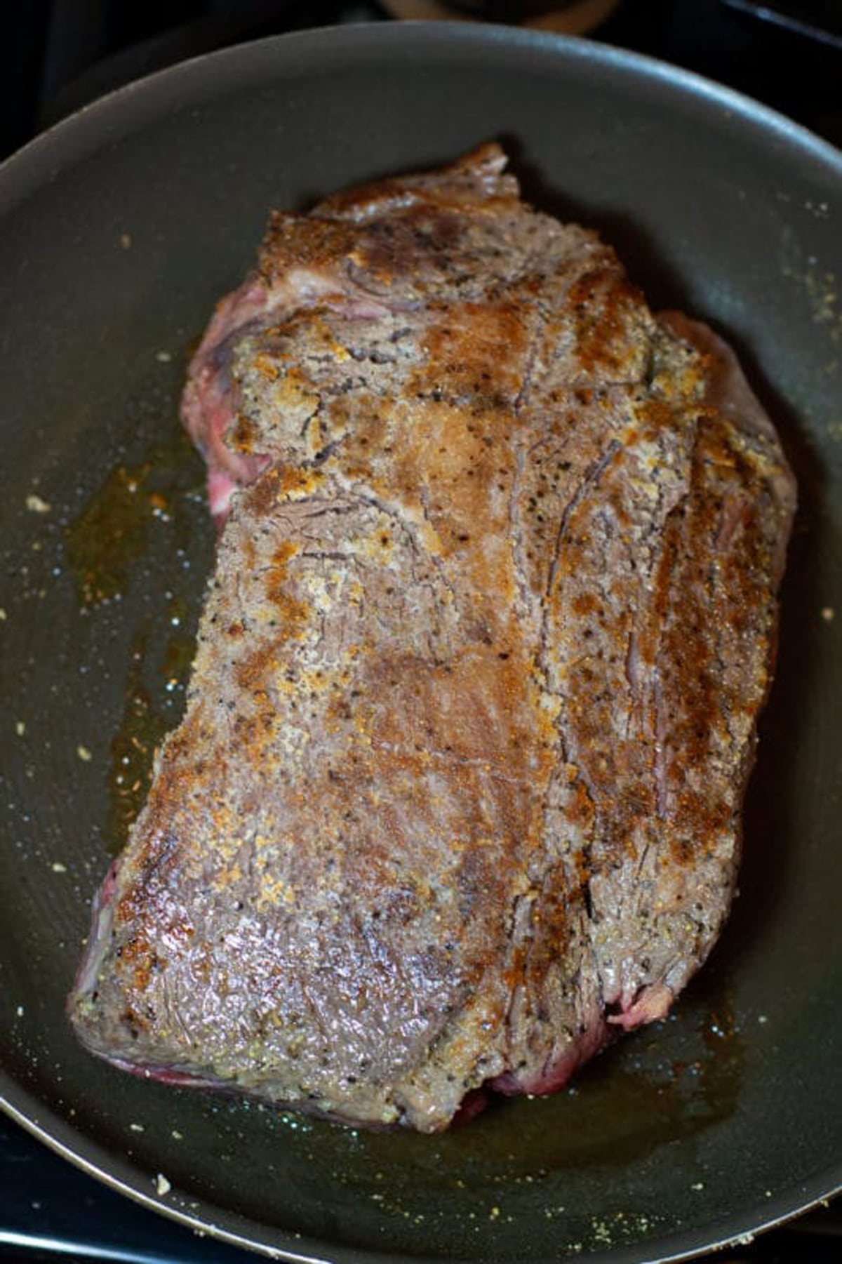 Searing a chuck roast in a skillet on stove top.