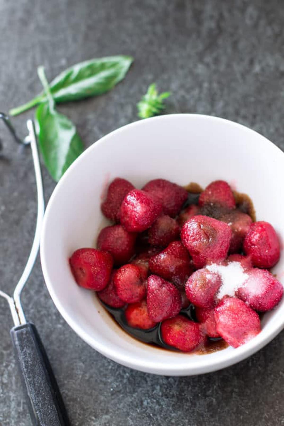 White bowl containing whole frozen strawberries, balsamic vinegar, and sugar.