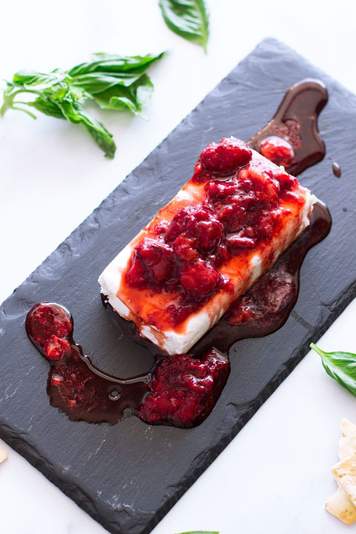 Strawberry sauce on a block of cream cheese, basil on table.