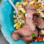 Fork full of flank steak topped with corn salsa and feta cheese.