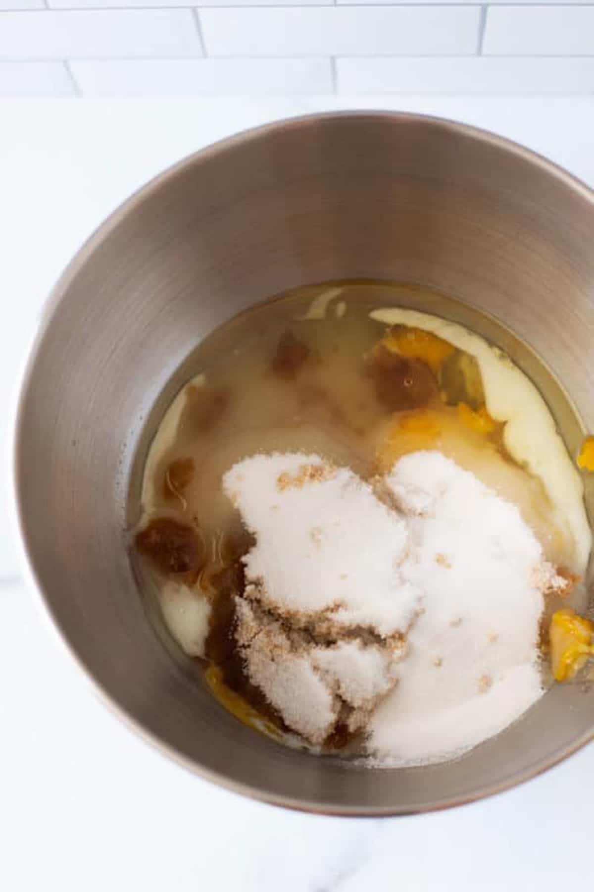 Silver bowl containing sugar, eggs, acorn squash puree, and oil.