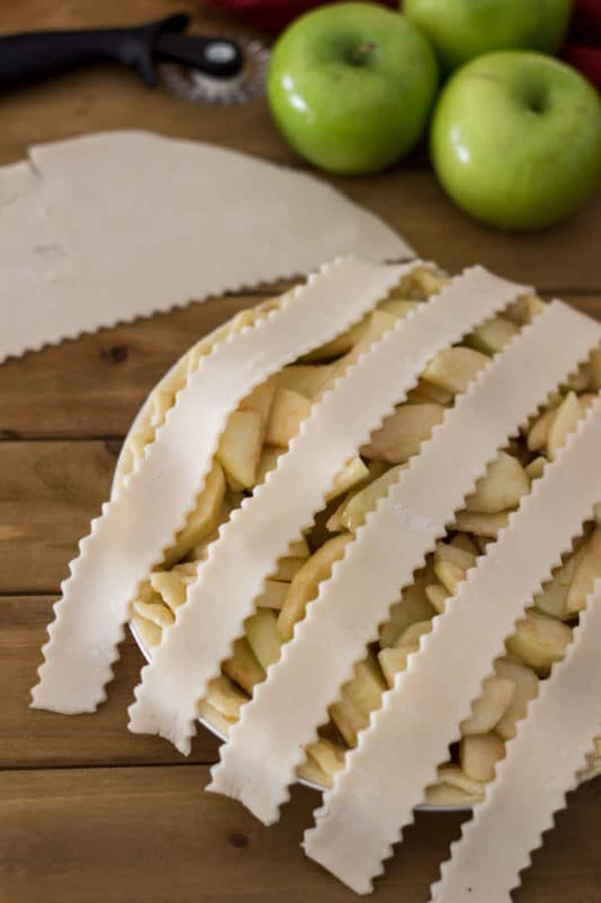 Pie covered with lattice pie crusts, granny smith apples on table.