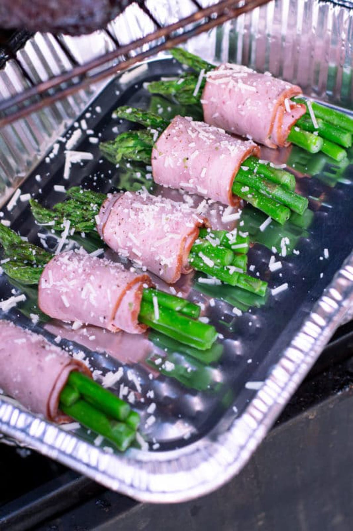 An aluminum pan with asparagus wrapped in bacon being placed in a smoker.