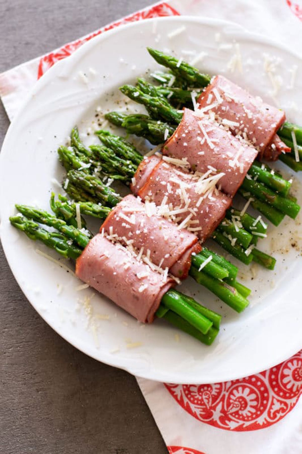 White plate containing asparagus spears wrapped in turkey bacon topped with Parmesan cheese.