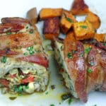 Bacon wrapped chicken breast stuffed with vegetables on white plate with roasted sweet potatoes.